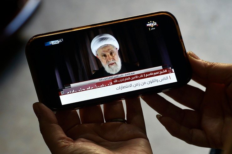 Una persona segue un comizio di Naim Qassem sullo schermo di uno smartphone 