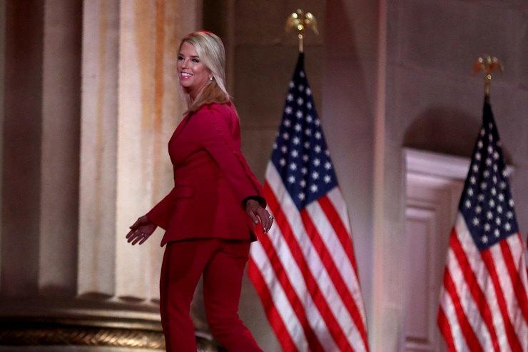 Pam Bondi cammina davanti a due bandiere degli Stati Uniti